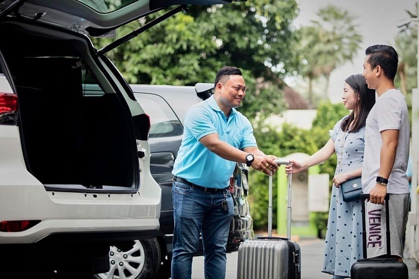 Private airport taxi driver assisting passengers with luggage for a comfortable airport transfer service in Thailand.